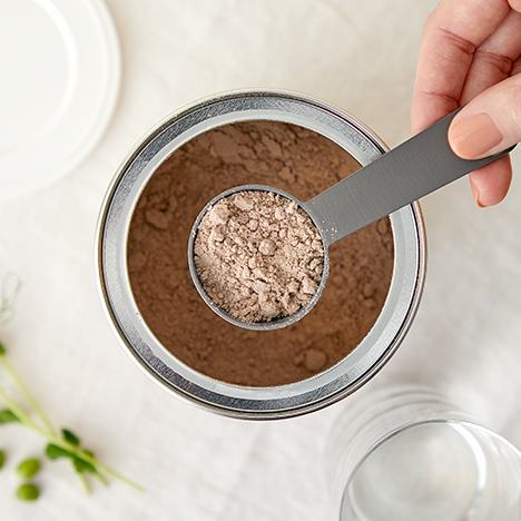 Một người đang cầm thìa trên một hộp bột.