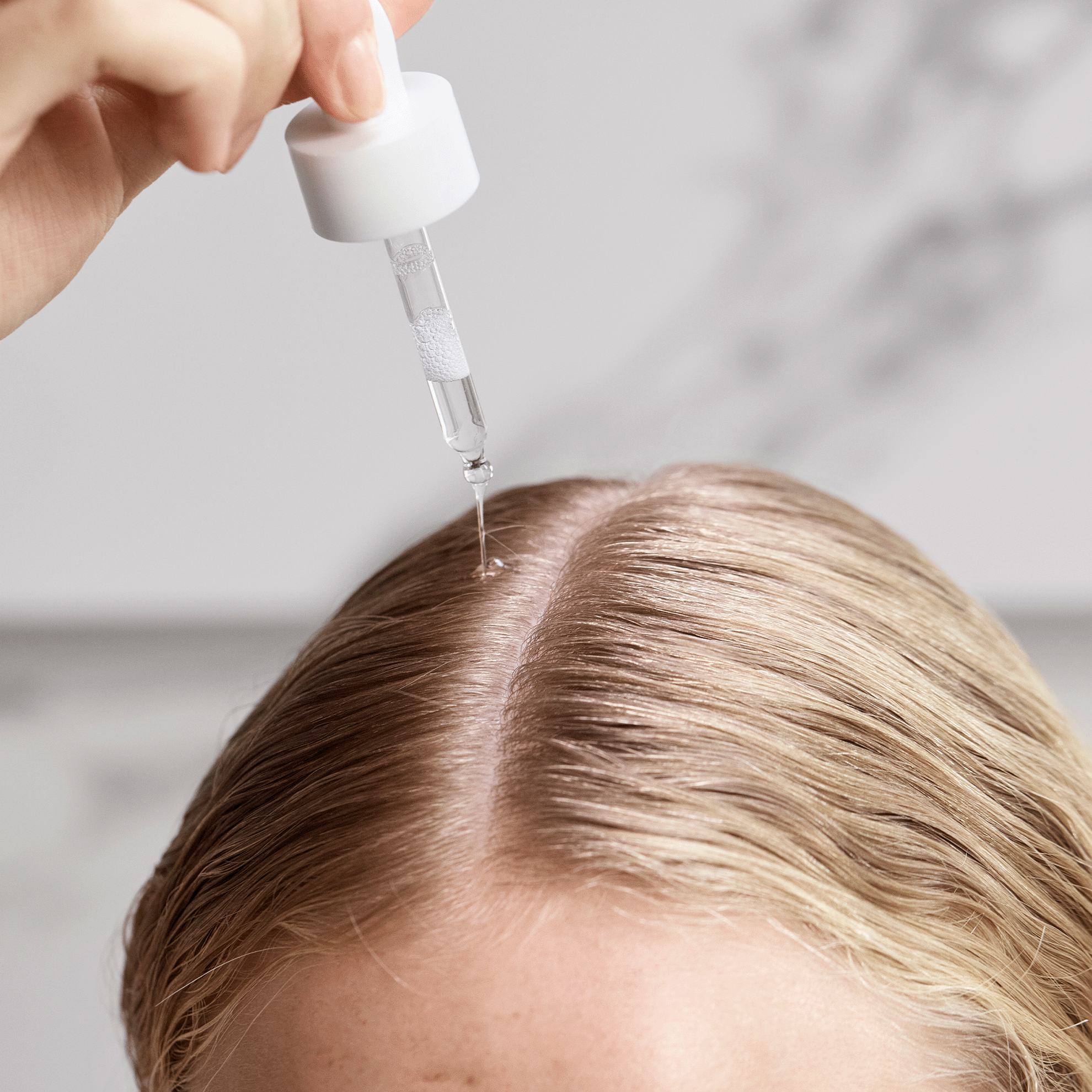 Một người đang sử dụng ống nhỏ giọt trên tóc của một phụ nữ.